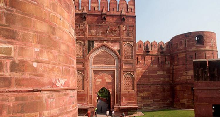 The impressive red-sandstone gateway and walls of Agra Fort tower above visitors entering through an arched doorway.