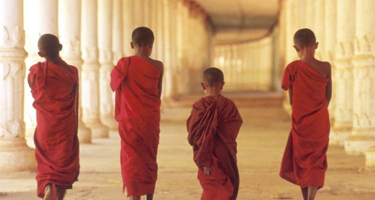 Quatre moines marchant dans un long couloir vêtus de robes rouges traditionnelles.