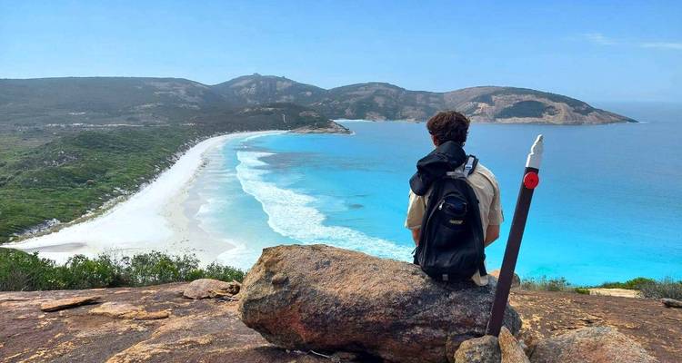 Een persoon die op een rots zit en uitkijkt over een kustlandschap.