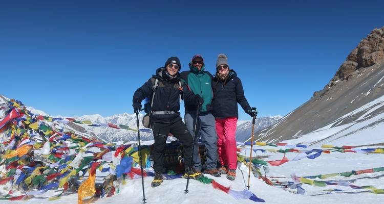 Three hikers standing with prayer flags in the snow-covered mountains.