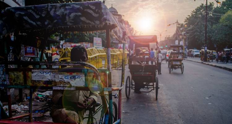 Rickshaws on a busy street during sunset.