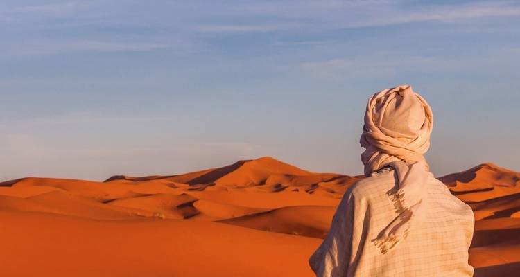 Eine Person in traditioneller Kleidung, die Sanddünen in einer Wüstenlandschaft überblickt.