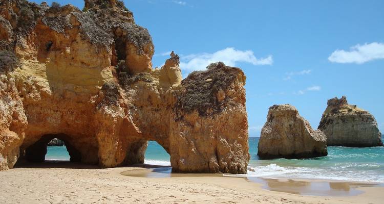 Côte rocheuse avec des arches naturelles et un rivage sablonneux.