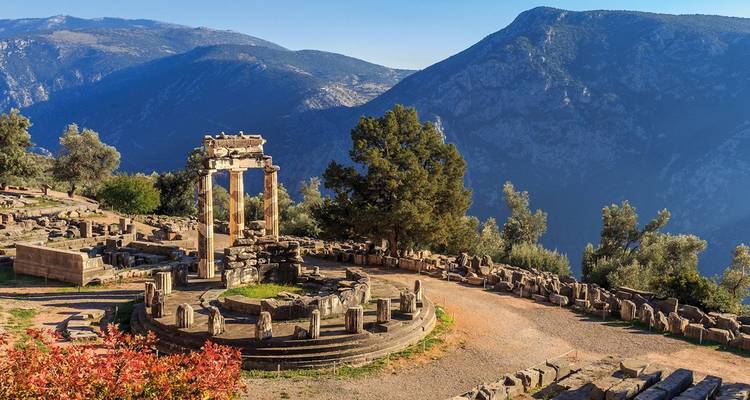 Antiguo santuario circular de Delfos rodeado de montañas escarpadas bajo un cielo azul despejado