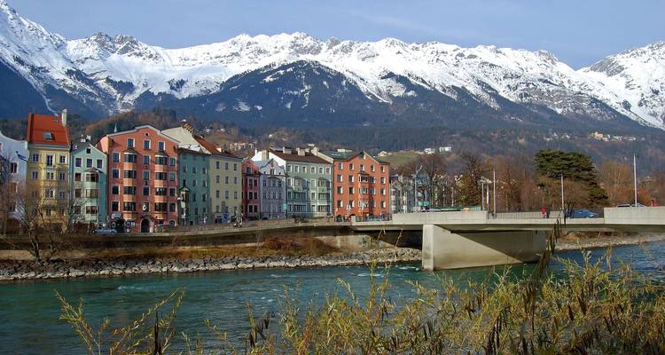 Bâtiments colorés le long d'une rivière avec une montagne enneigée en arrière-plan.