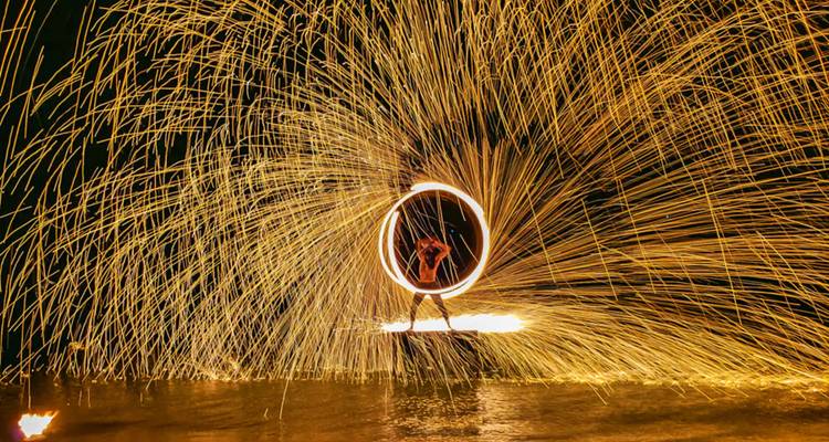 Fire performance with sparks flying, creating a ring of light on the beach.