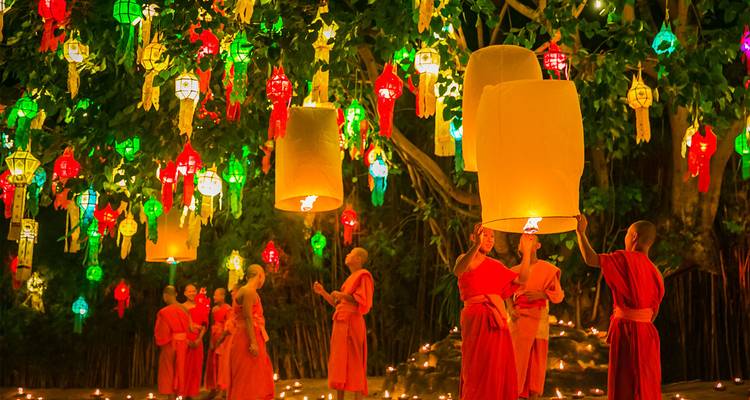 Monks launching sky lanterns among colorful hanging lanterns.