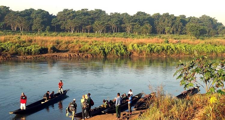 Des gens embarquant dans des canoës sur une rivière aux rives boisées.