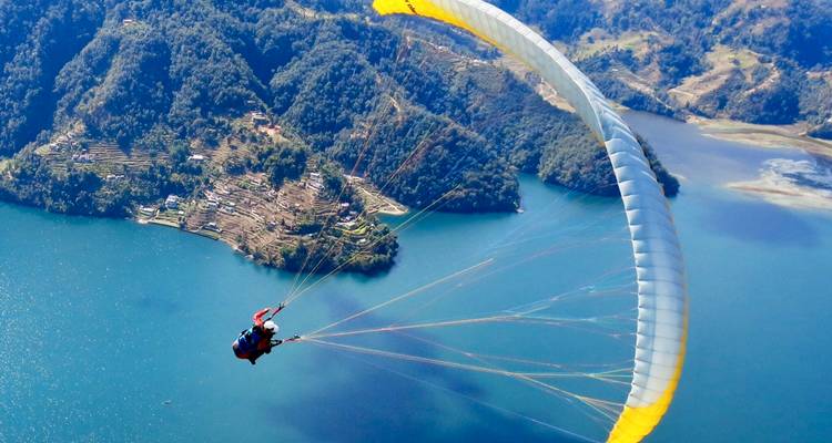 Personne faisant du parapente au-dessus d'un lac avec des collines en arrière-plan.