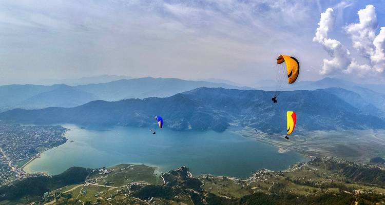 Plusieurs parapentistes planent au-dessus d'un vaste lac et d'une ville.