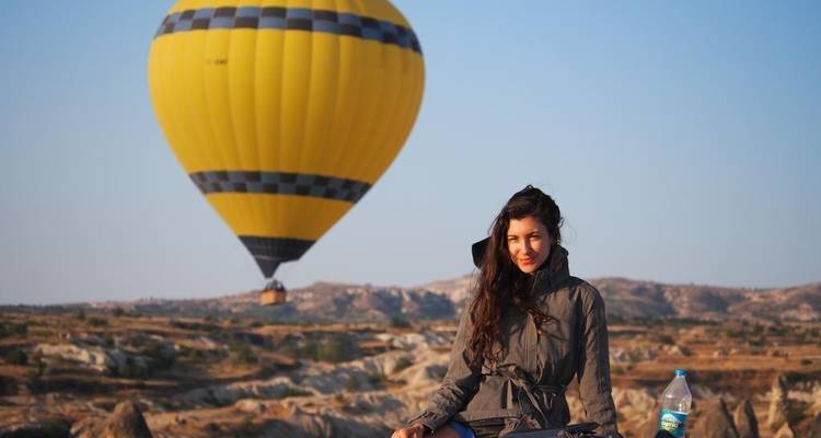 Woman sitting with a hot air balloon in the background at sunrise.