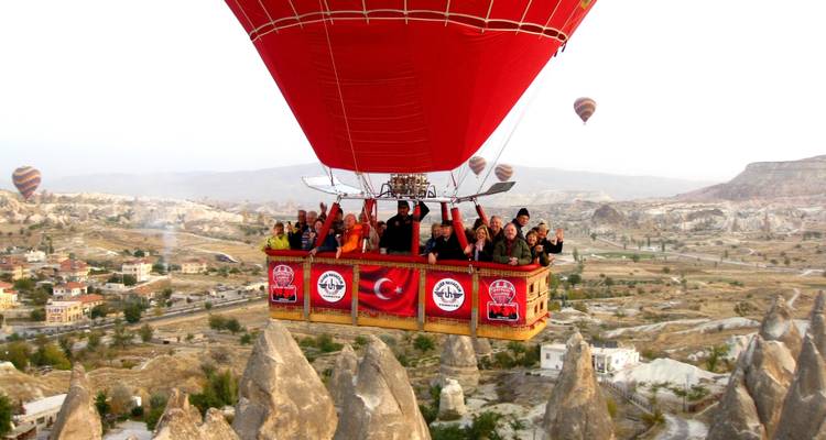 Group in a red hot air balloon basket flying over a rocky landscape.