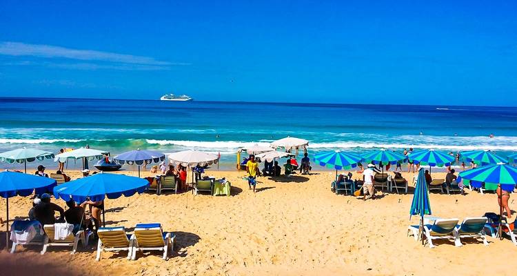 Strandszene mit Sonnenschirmen und entspannenden Menschen.