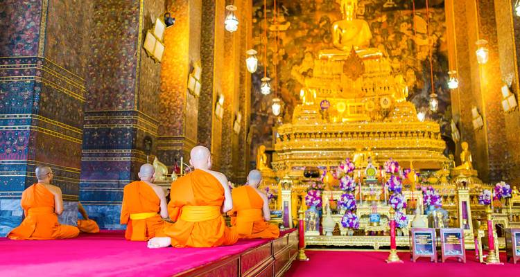 Monjes arrodillados frente a una estatua dorada dentro de un templo.