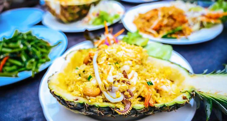 Arroz frito con piña servido en una piña ahuecada con otros platos.