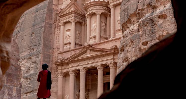 Facade of the ancient city of Petra with a visitor in the foreground.