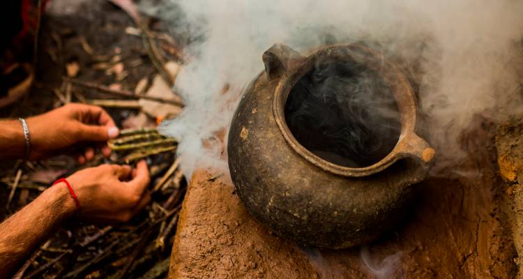 Hände, die wohlriechenden Rauch während eines traditionellen andinen Rituals über einen rustikalen Tontopf wehen.