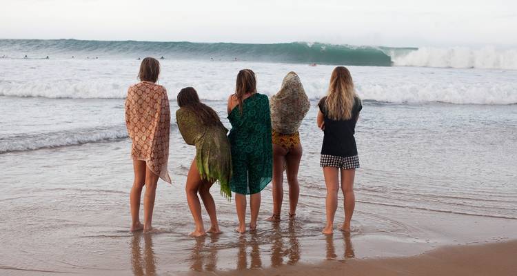 Vijf mensen die aan de waterkant staan en naar de golven kijken.