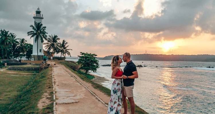 Een koppel dat elkaar omhelst bij een vuurtoren tijdens zonsondergang.