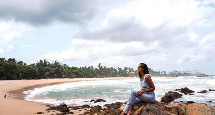 Een persoon die op rotsen zit met uitzicht op een strand en oceaan.