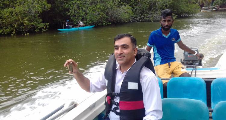 Twee mannen in een boot op een rivier met bomen en kajaks eromheen.