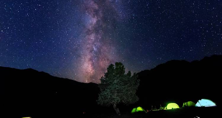 Milchstraße über einem Campingplatz mit Zelten, die in der Nacht leuchten.