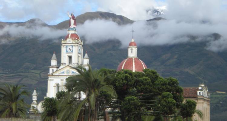 Een kerk met een rode koepel en een bergachtige achtergrond gedeeltelijk bedekt met wolken.