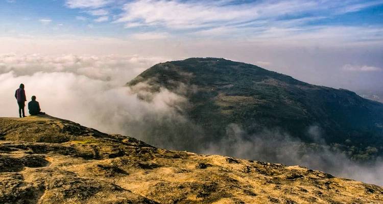 Twee mensen die op een klif zitten boven de wolken met uitzicht op de bergen.