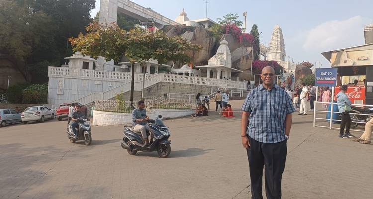 Man standing near a temple with scooters passing by.
