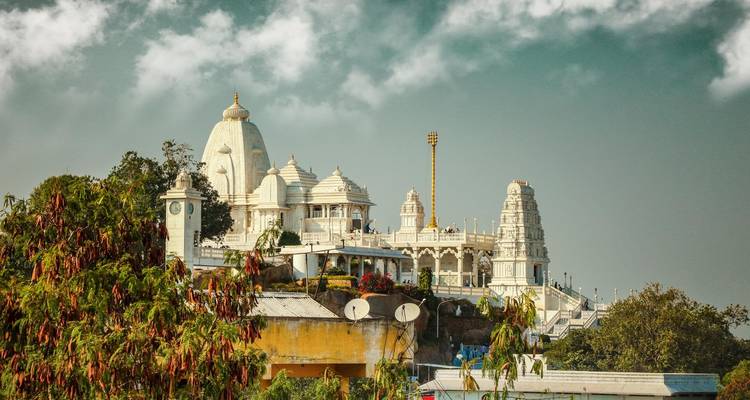 White temple complex on a hill with lush greenery and blue sky.