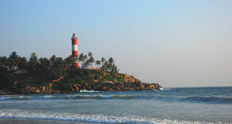 Kustlandschap met een vuurtoren en palmbomen aan zee.