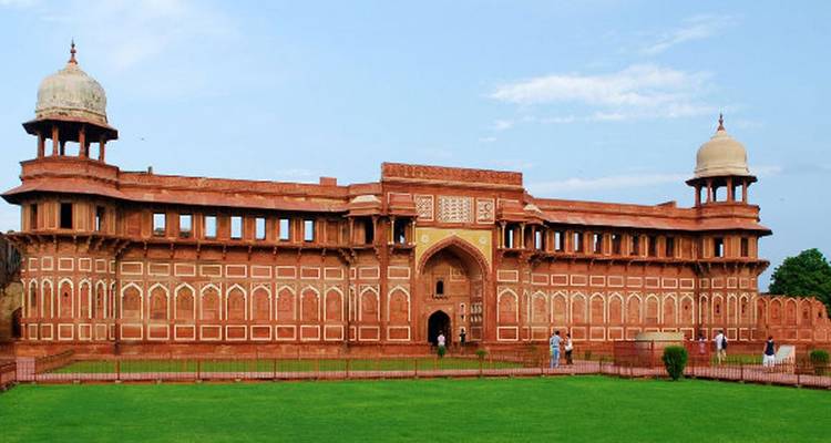 Fort with red sandstone walls and domes, surrounded by greenery.