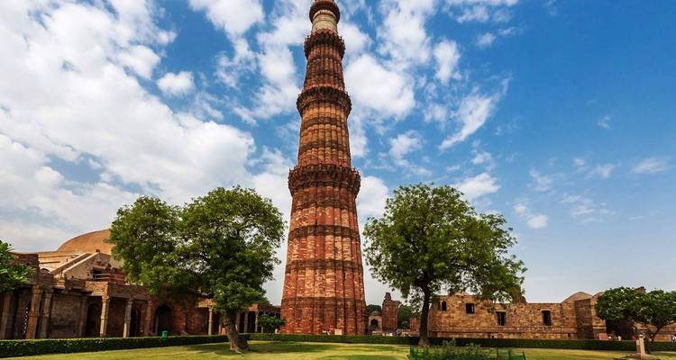 Tall stone minaret surrounded by trees and a partly cloudy sky.