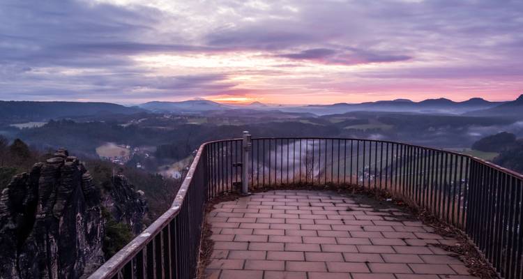 Viewing platform overlooking a misty valley at sunrise.