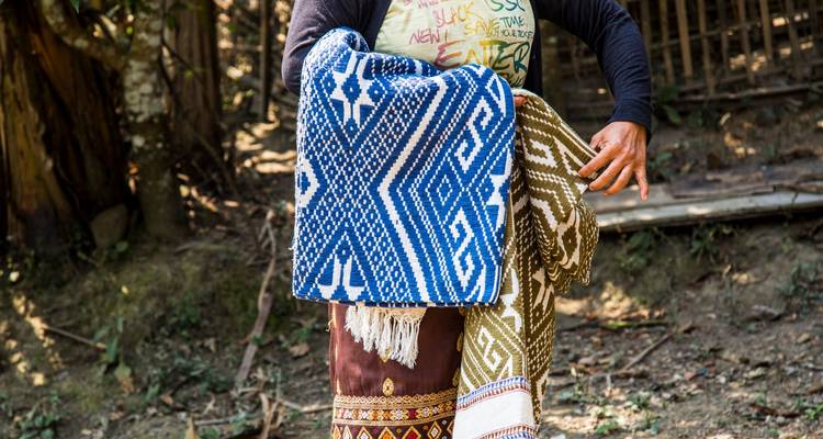 Person carrying colorful woven fabrics.