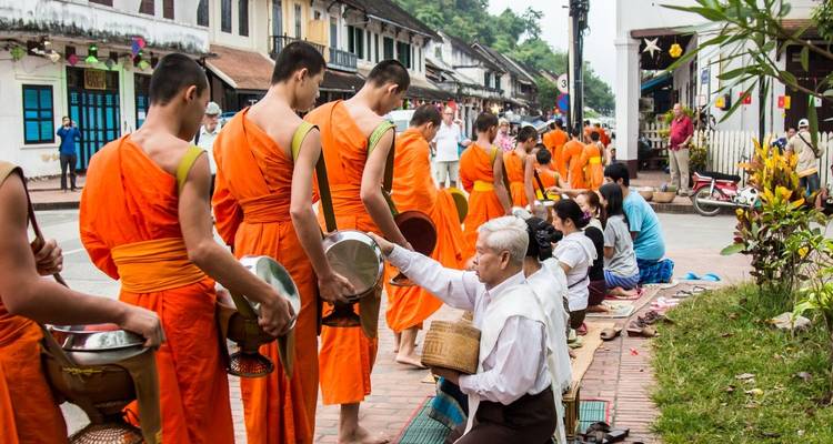 Monks in traditional orange robes collecting alms from locals.