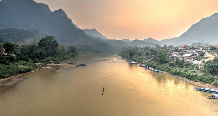 A wide river with boats and mountains on either side during an overcast sky.
