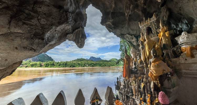 Statues in a temple cave overlooking a river and lush landscape.