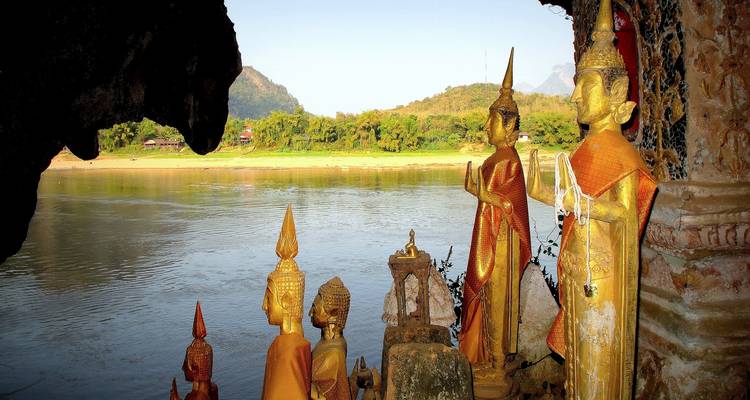 Golden Buddha statues in a cave with a river and jungle view.