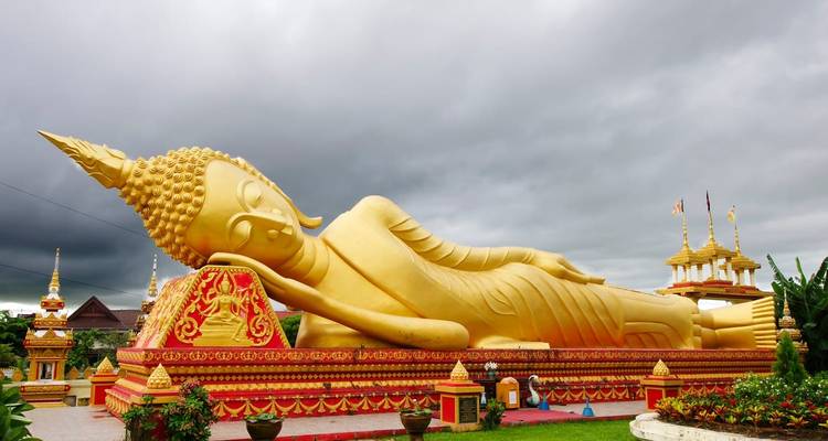 A large reclining golden Buddha statue against a cloudy sky.