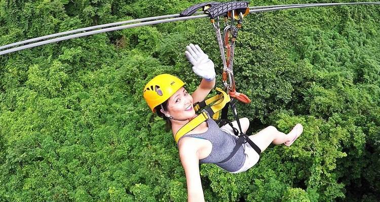 A person enjoying a zipline experience over a forest in a helmet and harness.