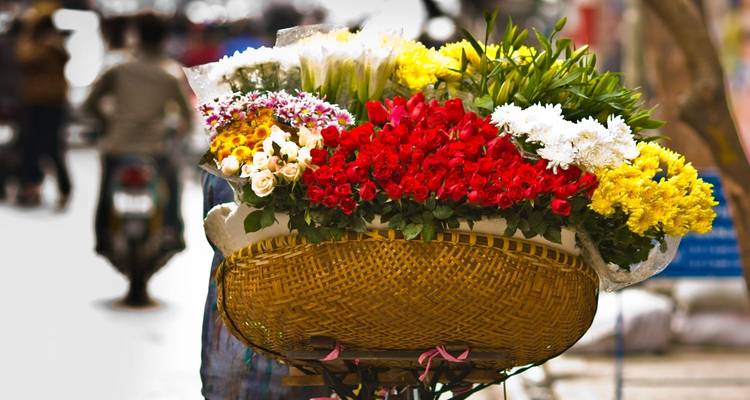 A bicycle laden with a large basket of vibrant flowers on a busy street.