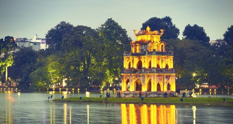 Illuminated pagoda reflecting in a lake at twilight.