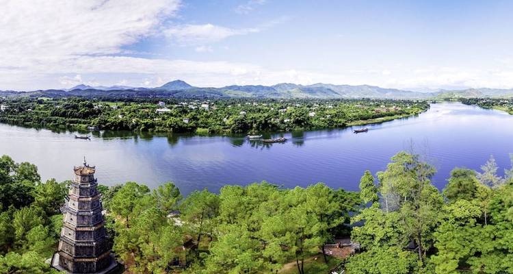 Panoramic view over a river with lush greenery and historical tower.