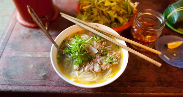 Bowl of noodle soup with ingredients on a table.