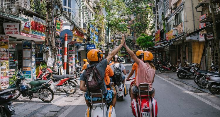 Tourists riding scooters, high-fiving in a lively street.