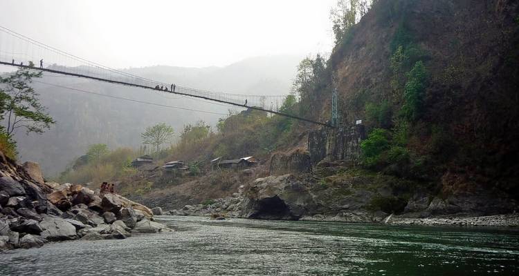 Hängebrücke über einen grünen Fluss mit Hügeln im Hintergrund.