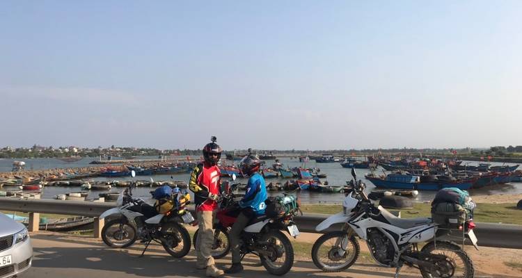 Motorcyclists posing near a harbor with numerous fishing boats.