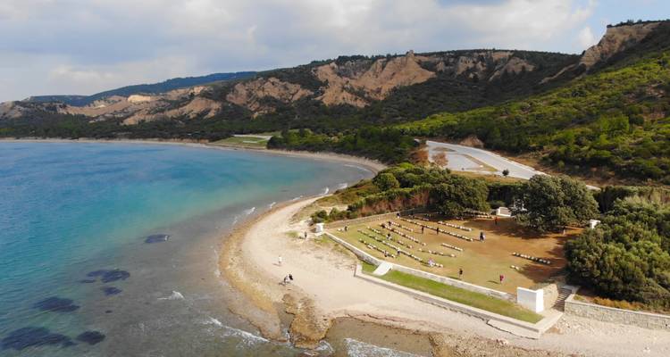 Vue aérienne d'un cimetière de guerre côtier et d'une vaste baie turquoise adossée à des collines verdoyantes