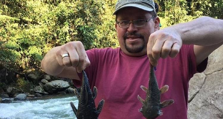 Man holding two fish in his hands with a river backdrop.